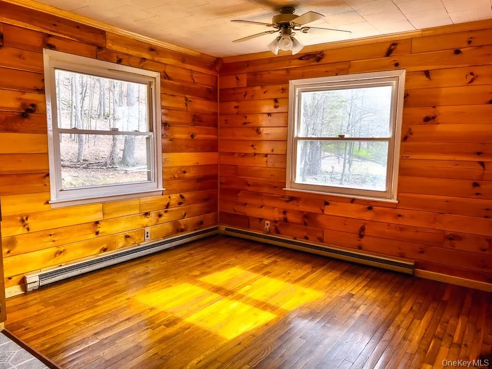 This room features hardwood floors and wood paneled walls, with two windows providing views of the natural surroundings This room features hardwood floors and wood paneled walls, with two windows providing views of the natural surroundings