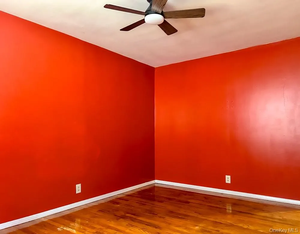 This room features vibrant red walls, polished hardwood flooring, and a ceiling fan with wooden blades This room features vibrant red walls, polished hardwood flooring, and a ceiling fan with wooden blades
