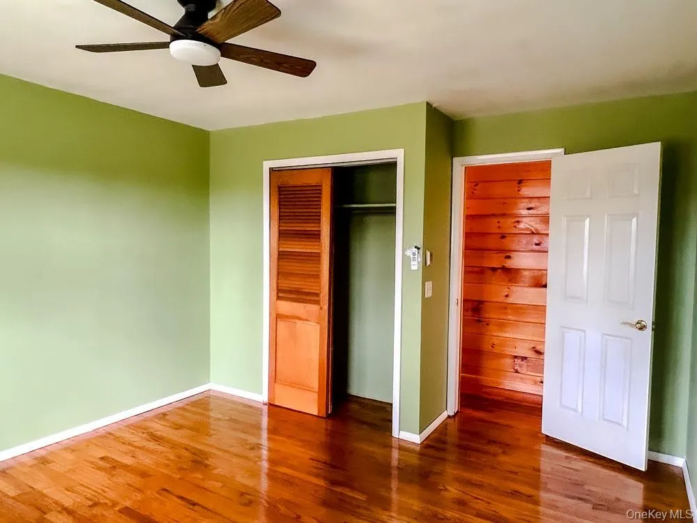This room features hardwood flooring, light green walls, a ceiling fan with light, and a closet with louvered bi-fold doors This room features hardwood flooring, light green walls, a ceiling fan with light, and a closet with louvered bi-fold doors