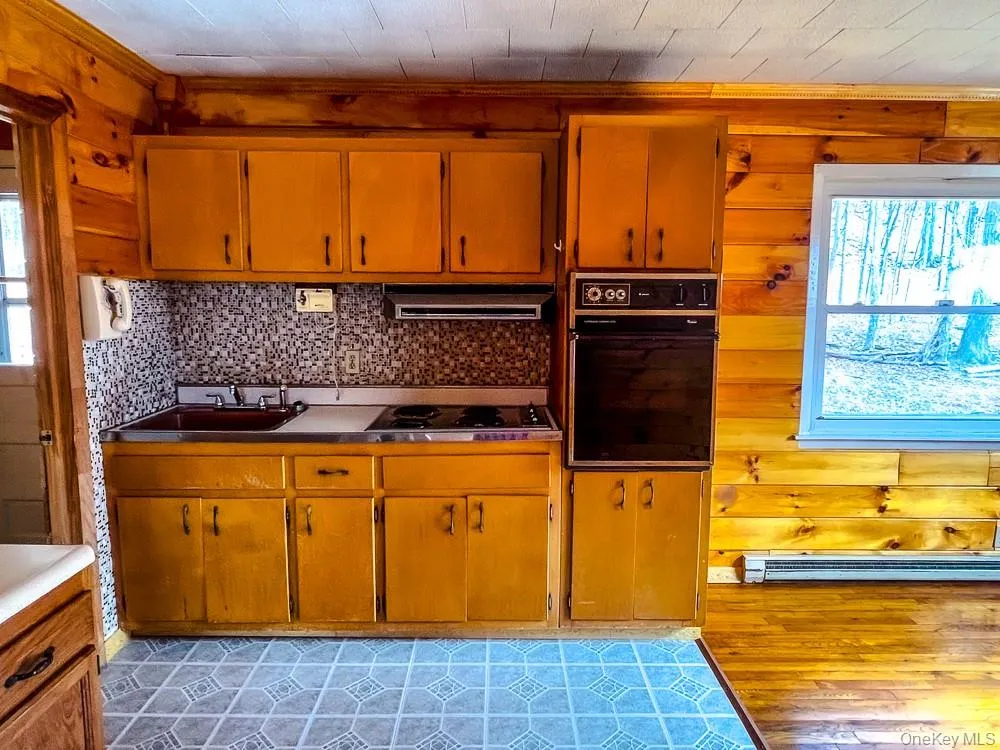 The kitchen features wood paneling, wood cabinetry, a built-in oven, and a window with an exterior view The kitchen features wood paneling, wood cabinetry, a built-in oven, and a window with an exterior view