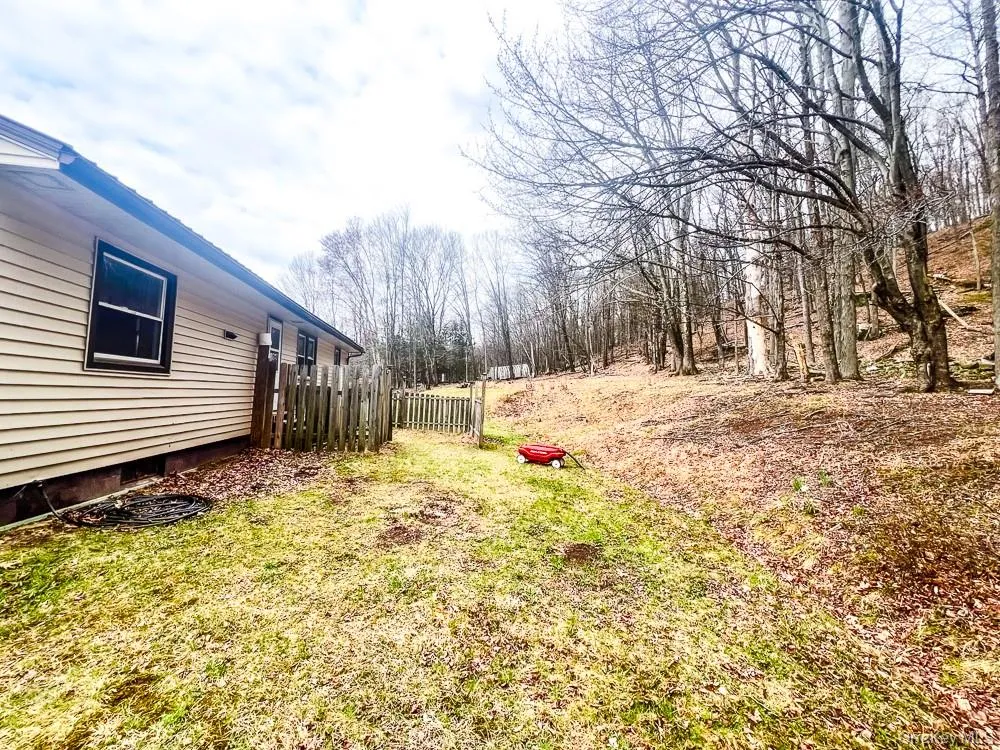 The property features a fenced yard with a gate, a sloped area, and mature trees in the background The property features a fenced yard with a gate, a sloped area, and mature trees in the background