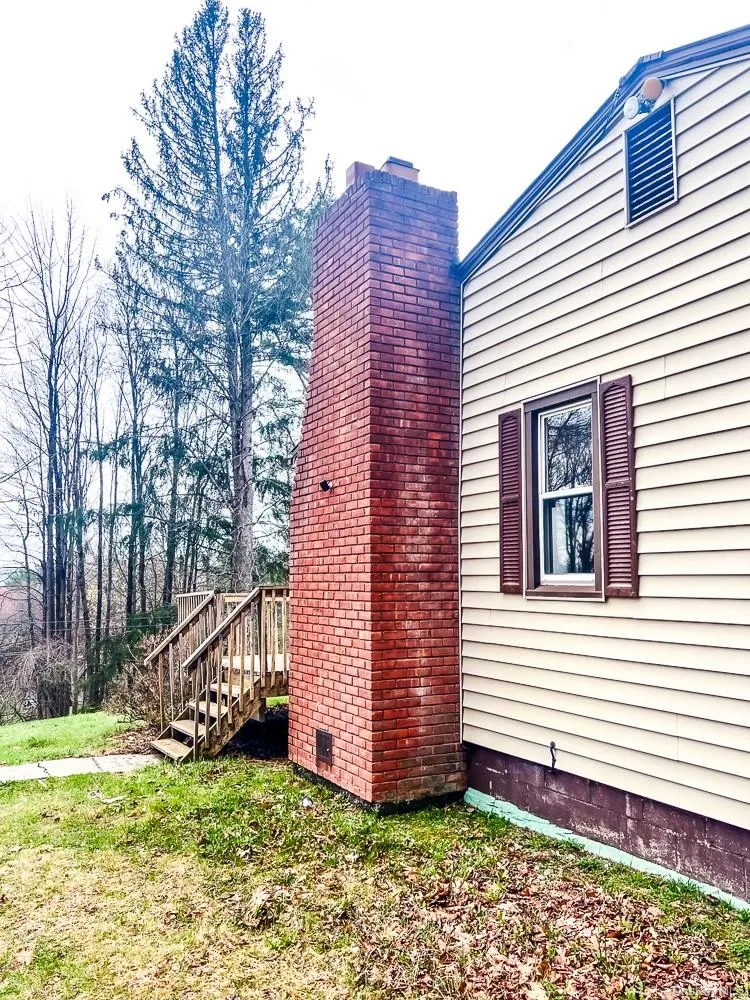 The property features a brick chimney, a window with louvered shutters, and exterior siding The property features a brick chimney, a window with louvered shutters, and exterior siding