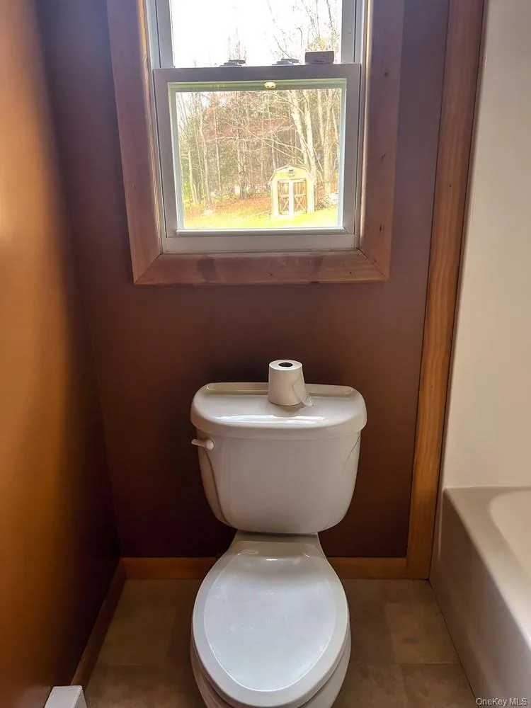 Bathroom featuring a window with natural wood trim, providing a view of the exterior with trees and a shed Bathroom featuring a window with natural wood trim, providing a view of the exterior with trees and a shed