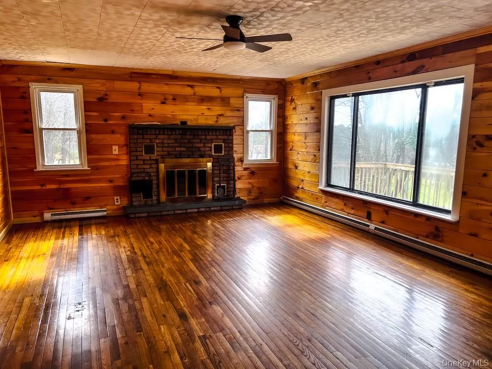 Living room featuring wood paneling, wood floors, and a brick fireplace Living room featuring wood paneling, wood floors, and a brick fireplace