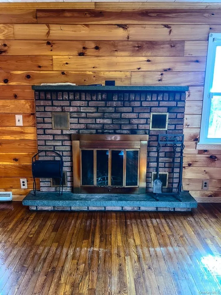 Living area featuring wood paneling, a brick fireplace with a stone hearth, and hardwood floors Living area featuring wood paneling, a brick fireplace with a stone hearth, and hardwood floors