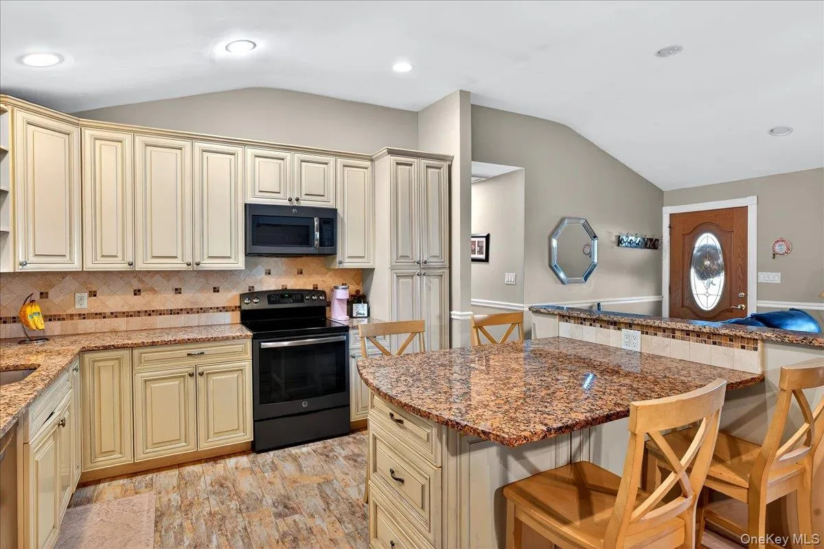 Kitchen with cream cabinetry, a kitchen bar, lofted ceiling, black / electric stove, and light stone countertops Kitchen with cream cabinetry, a kitchen bar, lofted ceiling, black / electric stove, and light stone countertops
