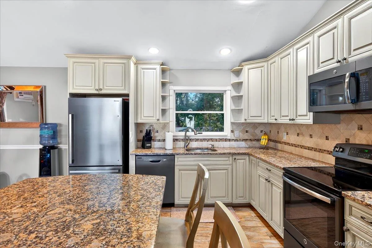 Kitchen featuring black appliances, open shelves, light stone countertops, cream cabinets, and recessed lighting Kitchen featuring black appliances, open shelves, light stone countertops, cream cabinets, and recessed lighting