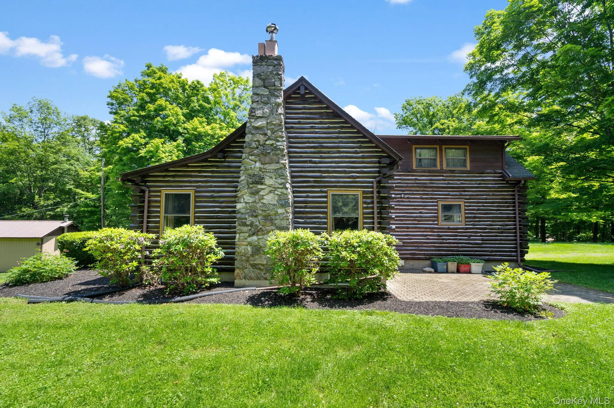 Rear view of property featuring a yard, log siding, a chimney, and a patio area Rear view of property featuring a yard, log siding, a chimney, and a patio area