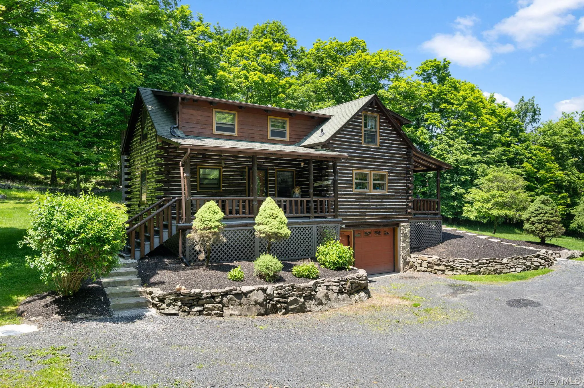 Cabin featuring log siding, an attached garage, covered porch, and asphalt driveway Cabin featuring log siding, an attached garage, covered porch, and asphalt driveway