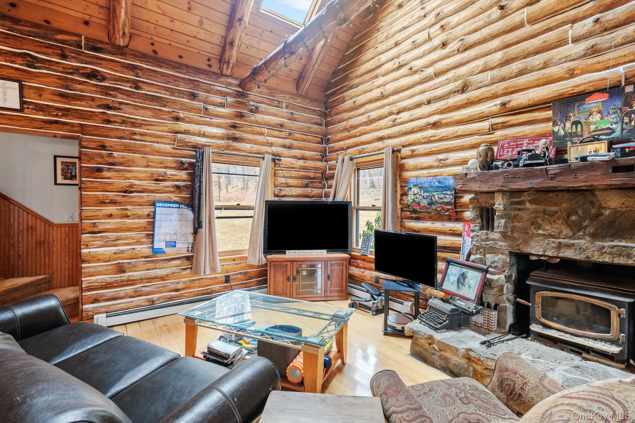 Living area featuring rustic walls, a wood stove, high vaulted ceiling, light wood finished floors, and a wood ceiling with exposed beams Living area featuring rustic walls, a wood stove, high vaulted ceiling, light wood finished floors, and a wood ceiling with exposed beams