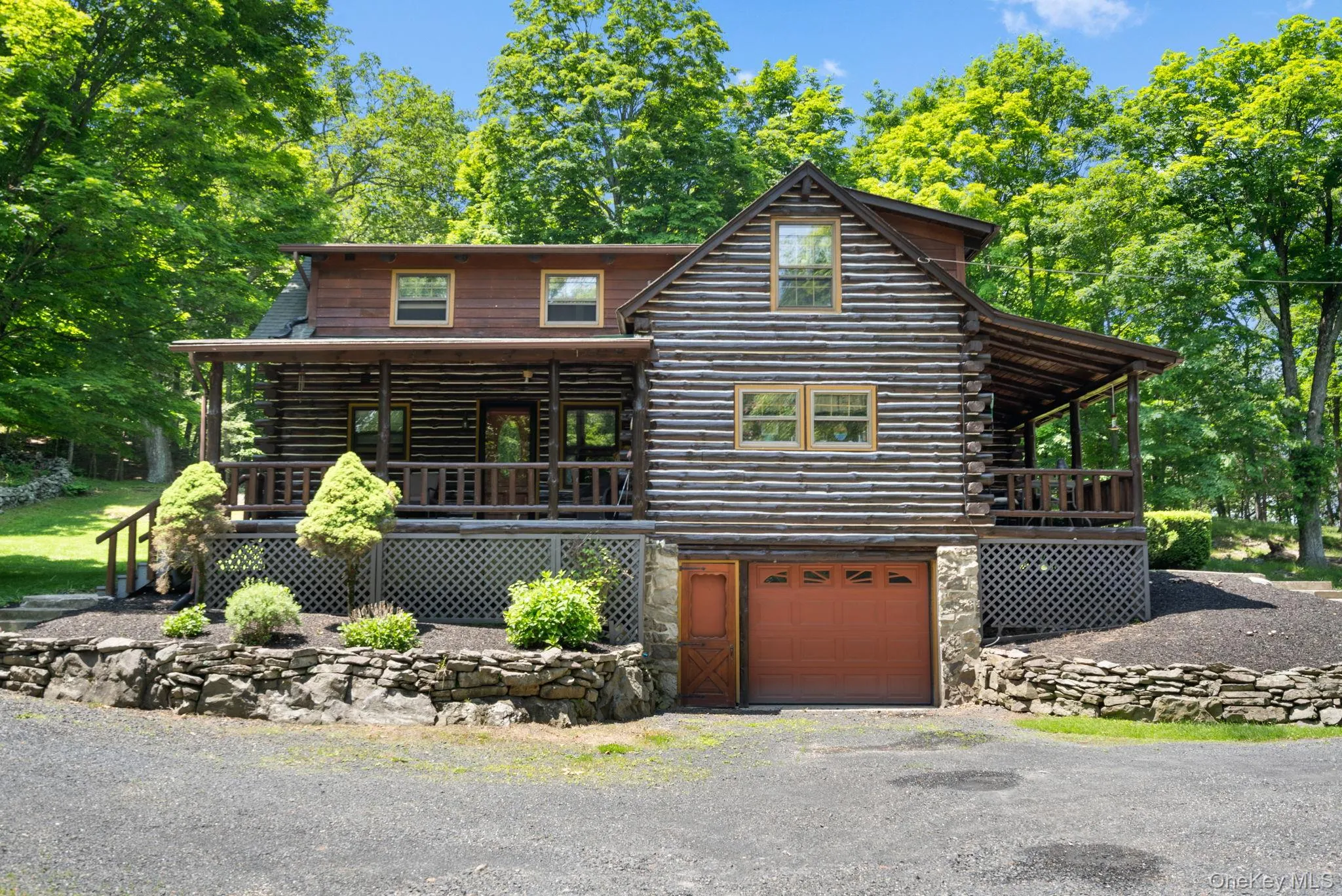 Log home featuring log siding, an attached garage, gravel driveway, a porch, and stone siding Log home featuring log siding, an attached garage, gravel driveway, a porch, and stone siding