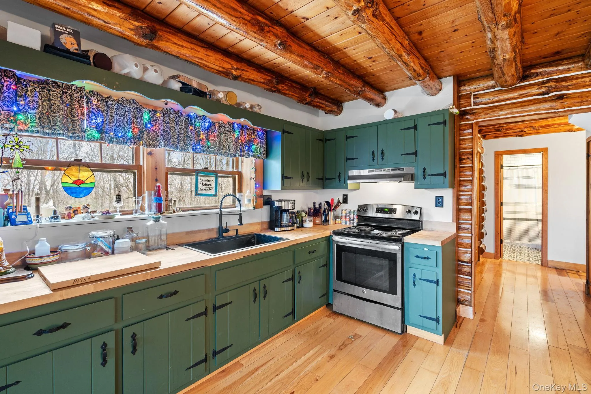 Kitchen with electric range, under cabinet range hood, a wooden ceiling with exposed beams, log walls, and wooden counters Kitchen with electric range, under cabinet range hood, a wooden ceiling with exposed beams, log walls, and wooden counters