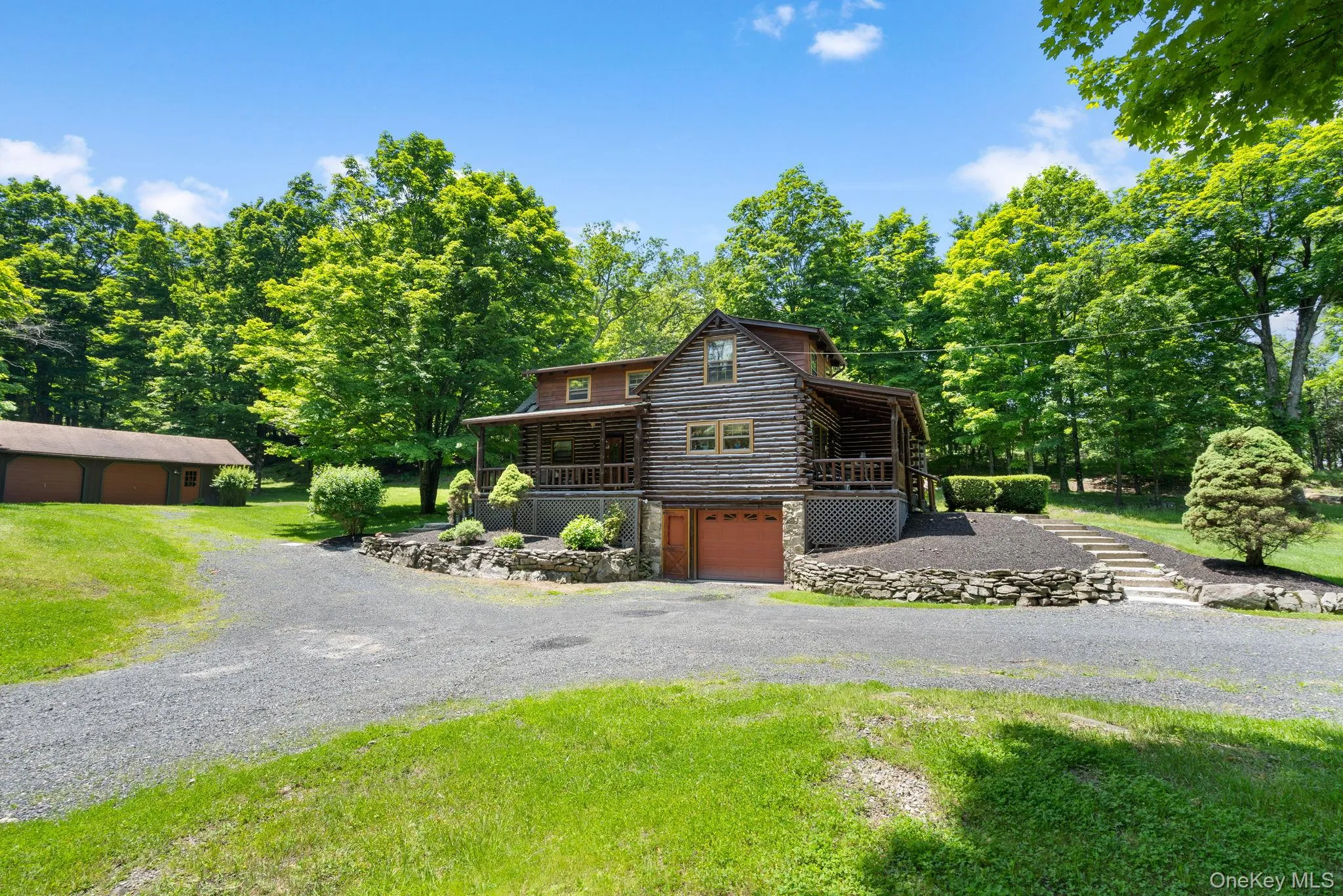 View of front of home featuring log siding, gravel driveway, a garage, stone siding, and a front yard View of front of home featuring log siding, gravel driveway, a garage, stone siding, and a front yard