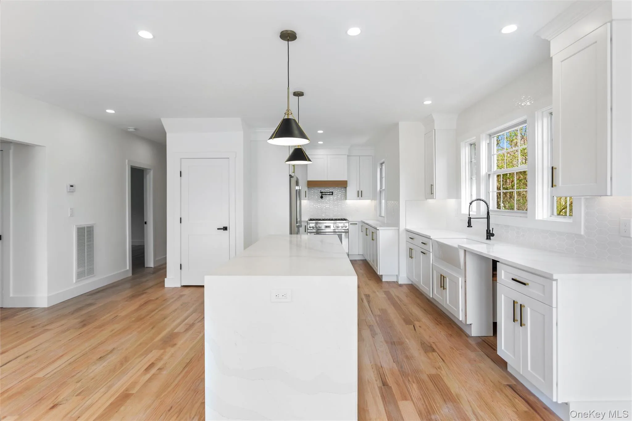 Modern kitchen featuring a large island, white cabinetry, integrated appliances, hardwood flooring, and a white tile backsplash Modern kitchen featuring a large island, white cabinetry, integrated appliances, hardwood flooring, and a white tile backsplash