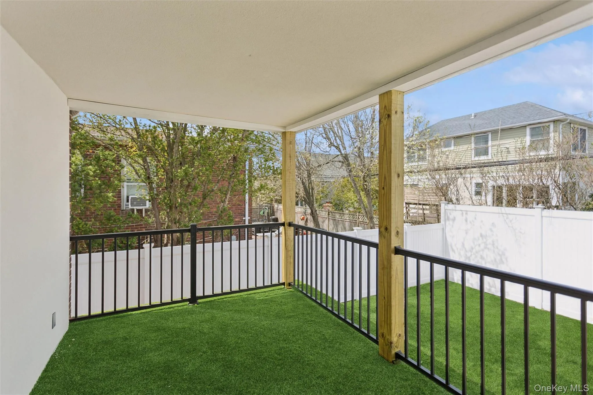 This outdoor area features a covered patio with a ceiling and a faux grass floor, enclosed by black metal railings This outdoor area features a covered patio with a ceiling and a faux grass floor, enclosed by black metal railings