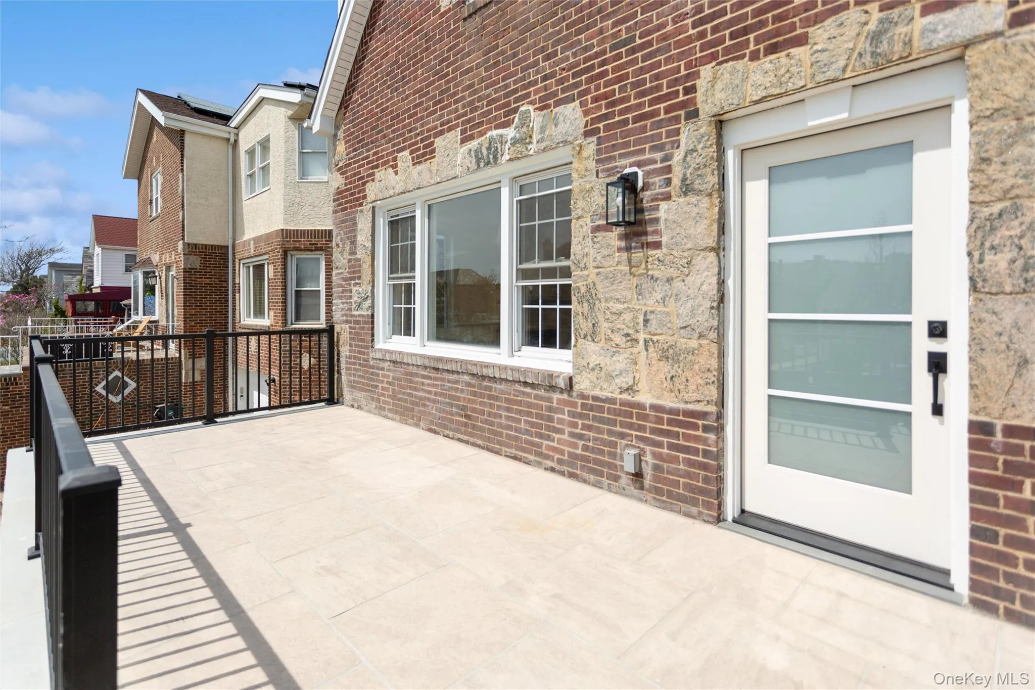 The property features a spacious outdoor patio with light-colored tile flooring and a black metal railing The property features a spacious outdoor patio with light-colored tile flooring and a black metal railing
