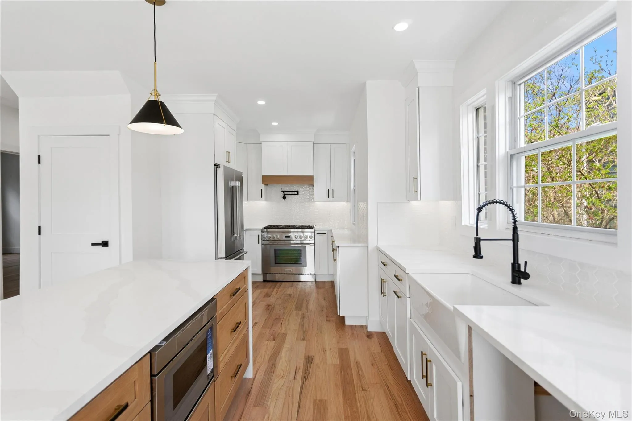 The kitchen features white cabinetry, hardwood floors, stainless steel appliances, and a kitchen island with a microwave The kitchen features white cabinetry, hardwood floors, stainless steel appliances, and a kitchen island with a microwave