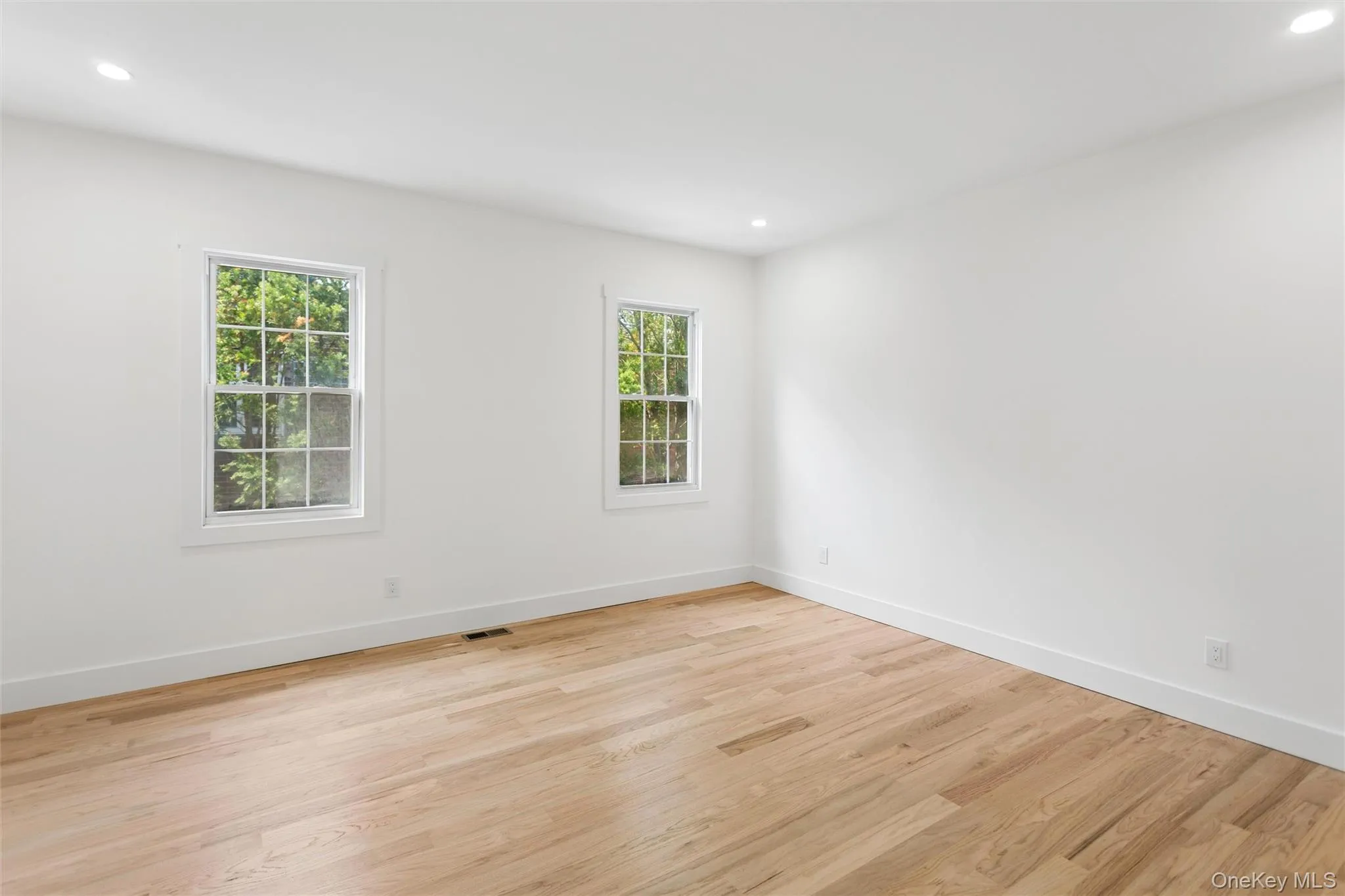 Bright room featuring light-toned hardwood flooring, white walls, and two windows with white frames Bright room featuring light-toned hardwood flooring, white walls, and two windows with white frames