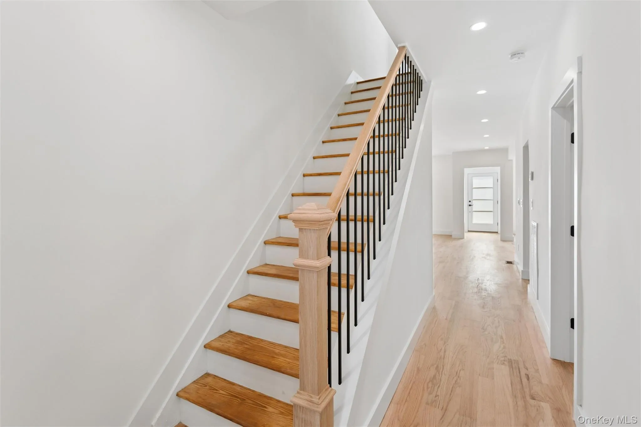 The entry hall features light hardwood flooring, a staircase with light wood treads and a black metal railing, and recessed lighting The entry hall features light hardwood flooring, a staircase with light wood treads and a black metal railing, and recessed lighting
