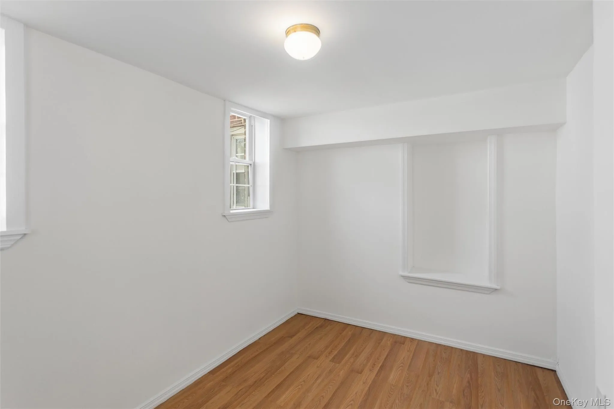 Room featuring hardwood flooring, white walls, and two windows allowing for natural light Room featuring hardwood flooring, white walls, and two windows allowing for natural light