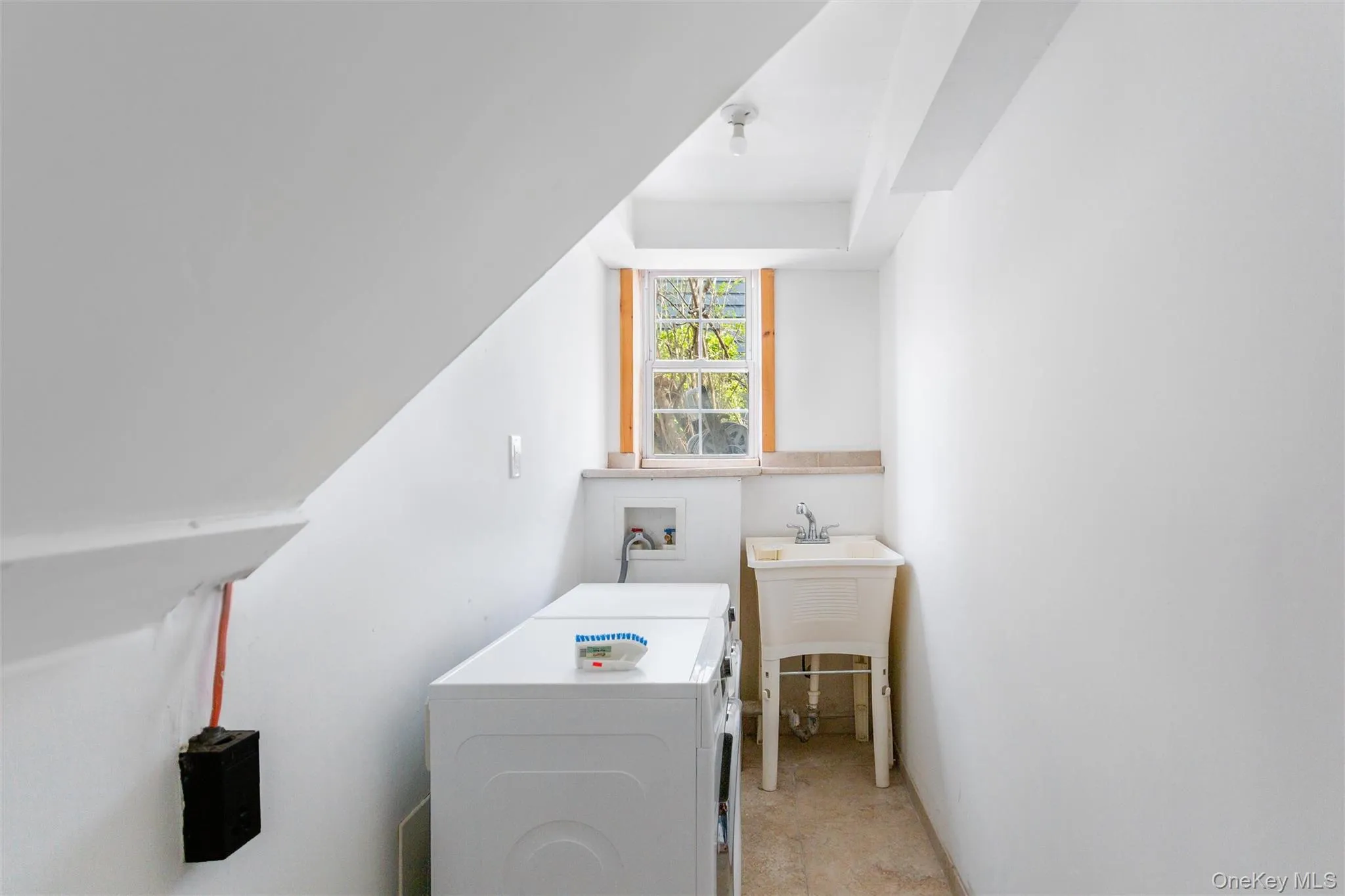 Practical laundry area featuring a utility sink, two laundry machines, and a window providing natural light Practical laundry area featuring a utility sink, two laundry machines, and a window providing natural light