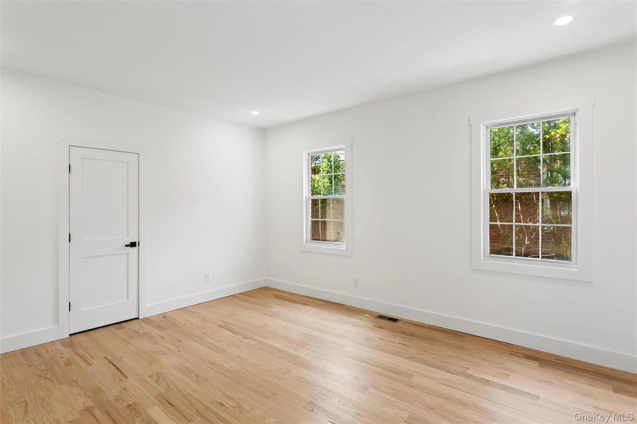 The room features light wood flooring, white walls, and two windows with white trim The room features light wood flooring, white walls, and two windows with white trim