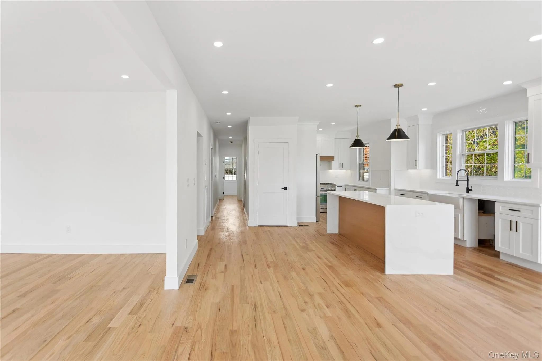 Open concept living area featuring light-toned hardwood floors, recessed lighting, and a kitchen with white cabinetry, a large island with a light wood base, and black pendant lights Open concept living area featuring light-toned hardwood floors, recessed lighting, and a kitchen with white cabinetry, a large island with a light wood base, and black pendant lights