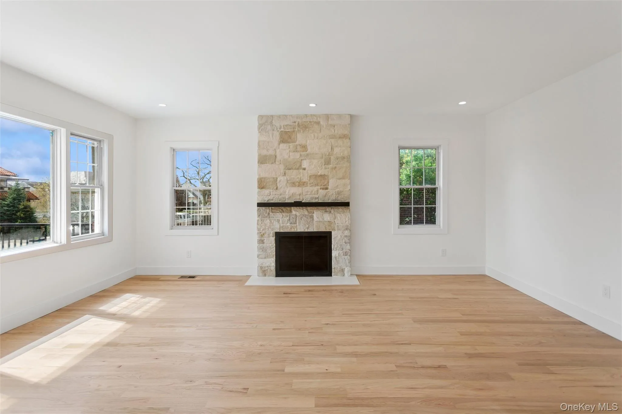 This inviting room features hardwood floors, a stone fireplace with a dark mantel, and recessed lighting This inviting room features hardwood floors, a stone fireplace with a dark mantel, and recessed lighting