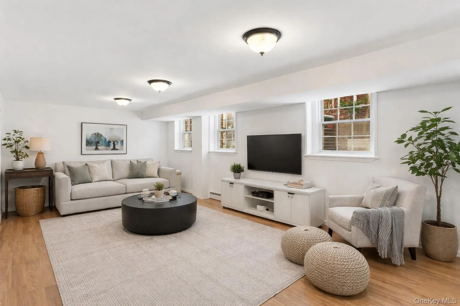 Staged Photo Spacious living area downstairs featuring light wood flooring, recessed lighting, and windows providing natural light Staged Photo Spacious living area downstairs featuring light wood flooring, recessed lighting, and windows providing natural light