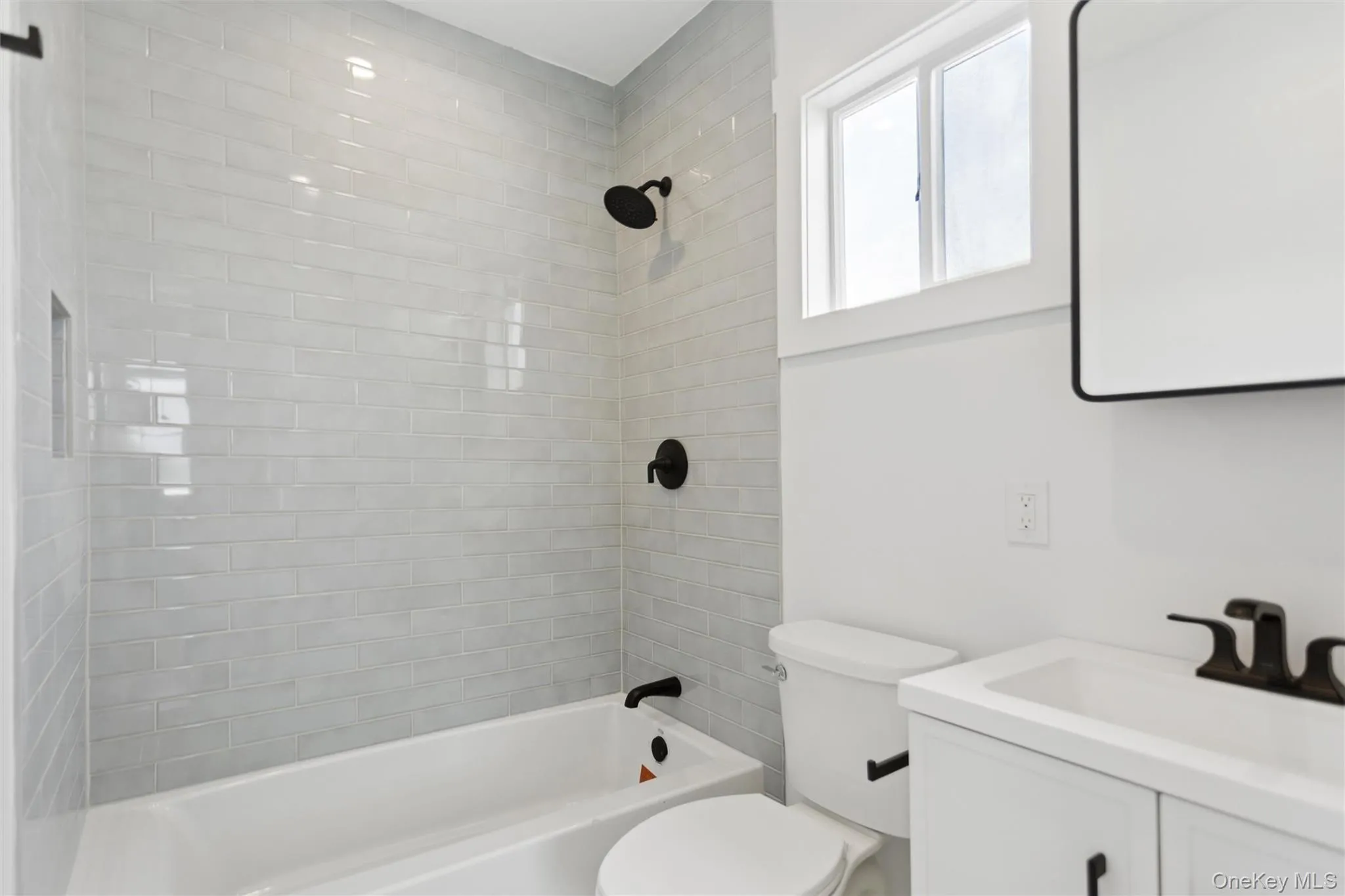 Bathroom featuring white subway tile in the shower, a window providing natural light, a white vanity with white countertop, and a black framed mirror Bathroom featuring white subway tile in the shower, a window providing natural light, a white vanity with white countertop, and a black framed mirror