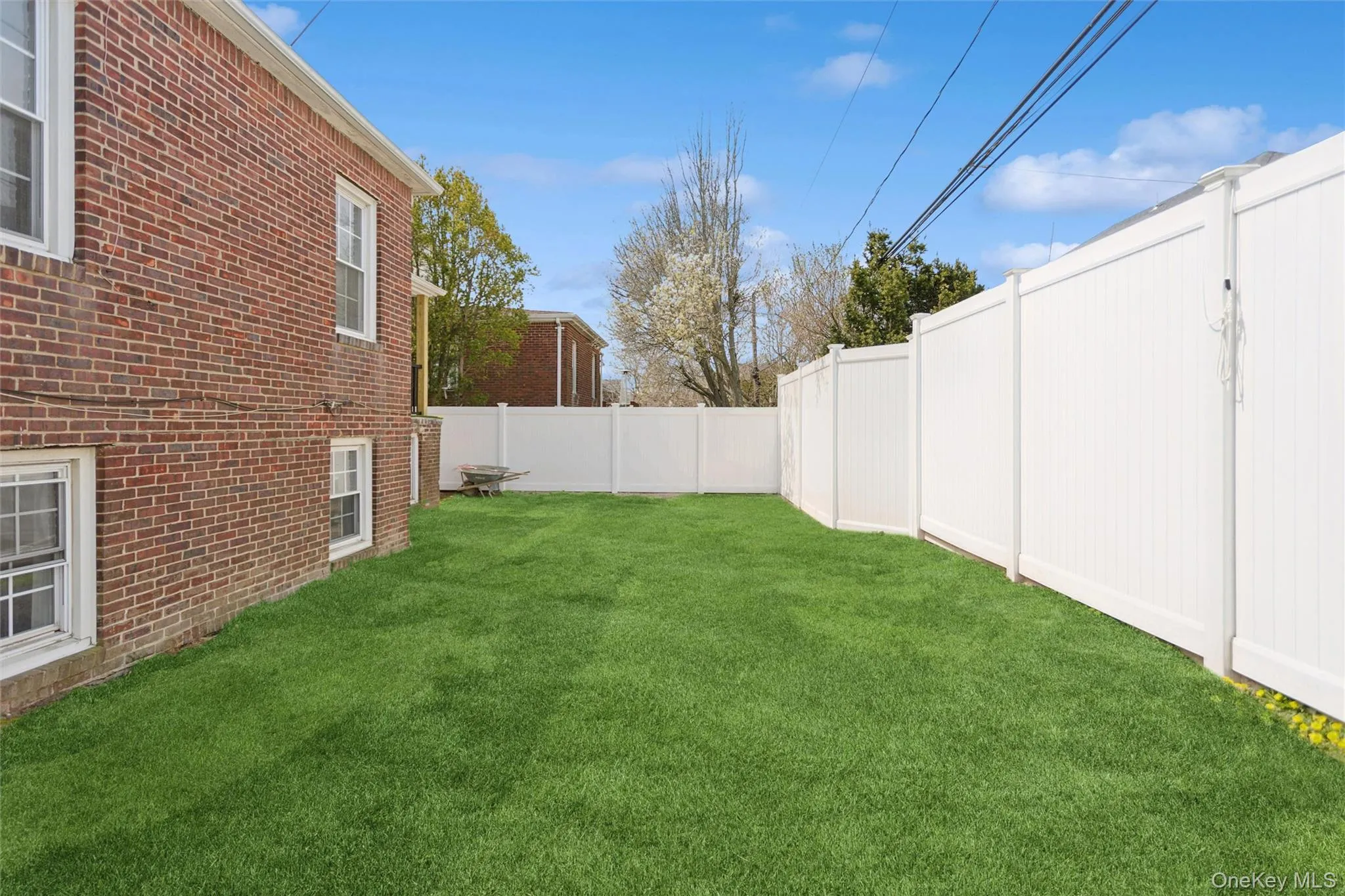 The property features a brick exterior with white-framed windows, a well-maintained lawn, and a white privacy fence The property features a brick exterior with white-framed windows, a well-maintained lawn, and a white privacy fence