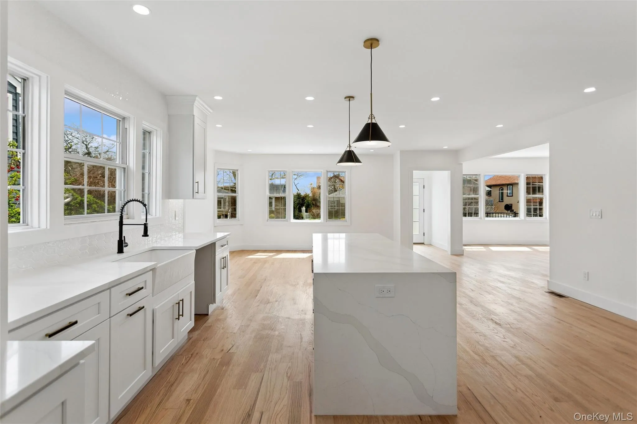 The kitchen features a large center island with a quartz countertop, white cabinetry with black hardware, a farmhouse sink with a black faucet, and hardwood flooring The kitchen features a large center island with a quartz countertop, white cabinetry with black hardware, a farmhouse sink with a black faucet, and hardwood flooring