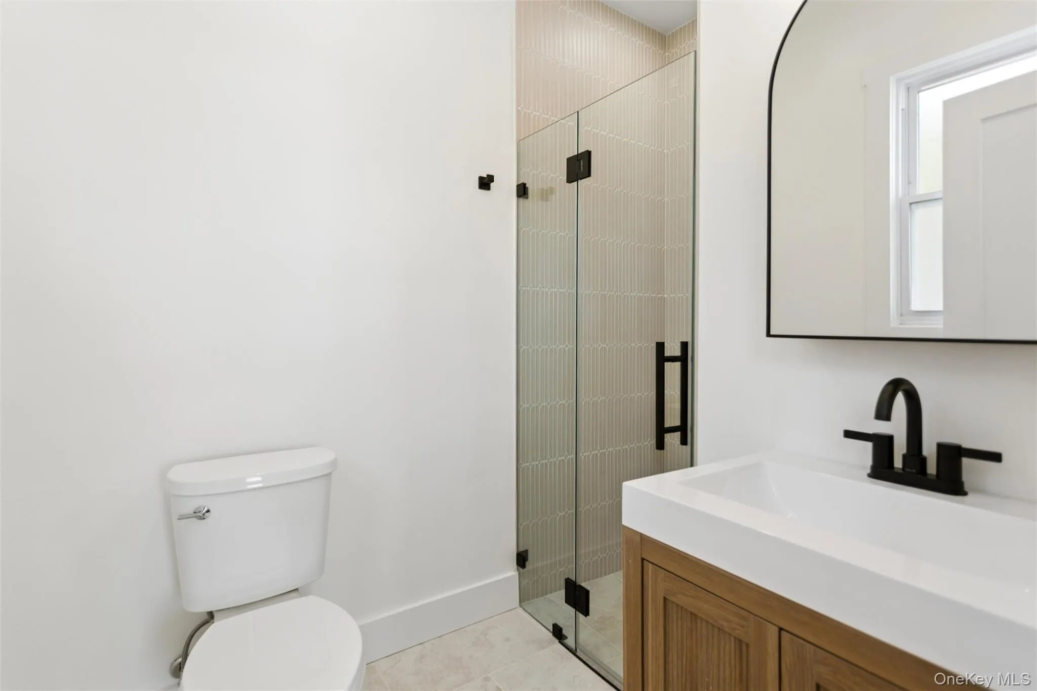 The bathroom features a modern vanity with a white countertop and dark-toned faucet, a glass-enclosed shower with tiled walls, and a white toilet The bathroom features a modern vanity with a white countertop and dark-toned faucet, a glass-enclosed shower with tiled walls, and a white toilet