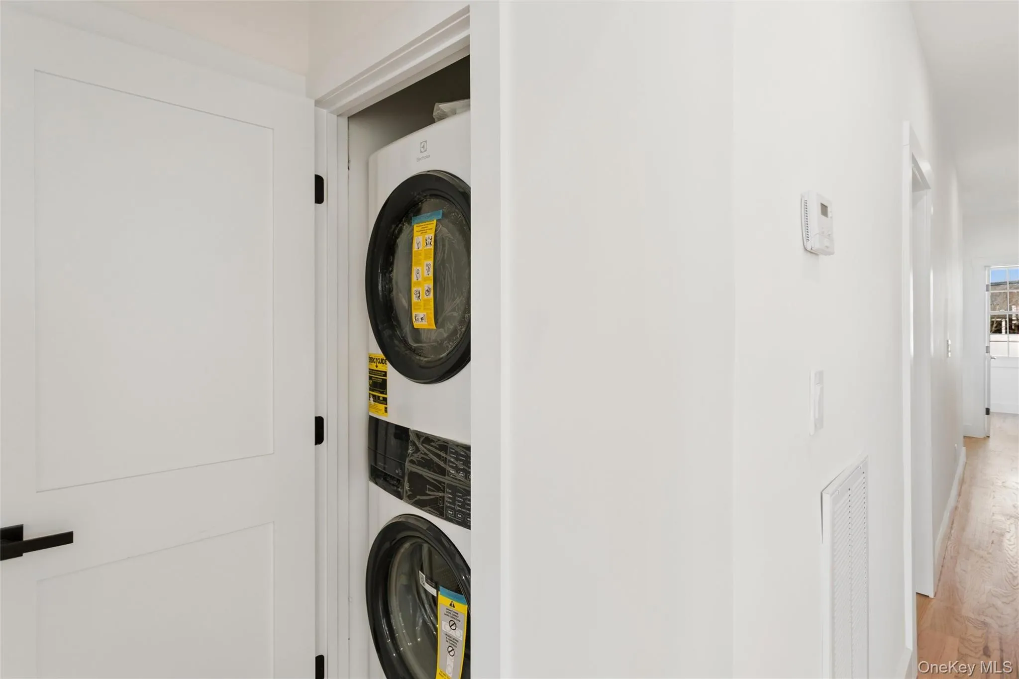 Convenient in-unit laundry featuring a stacked washer and dryer, located behind a white paneled door with a black handle Convenient in-unit laundry featuring a stacked washer and dryer, located behind a white paneled door with a black handle
