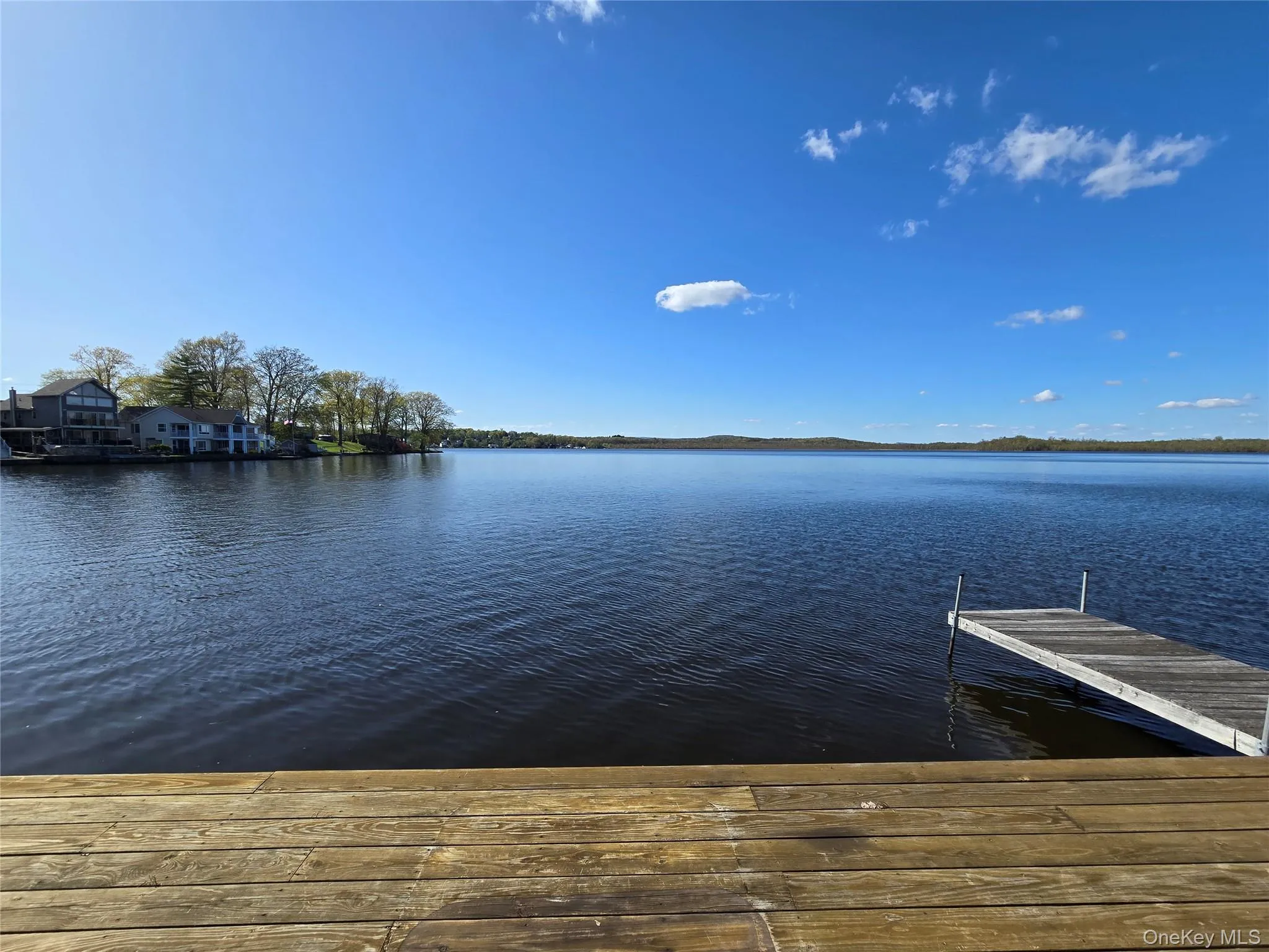 Expansive lakefront property featuring a wooden dock, a broad body of water, and a tree-lined distant shore Expansive lakefront property featuring a wooden dock, a broad body of water, and a tree-lined distant shore