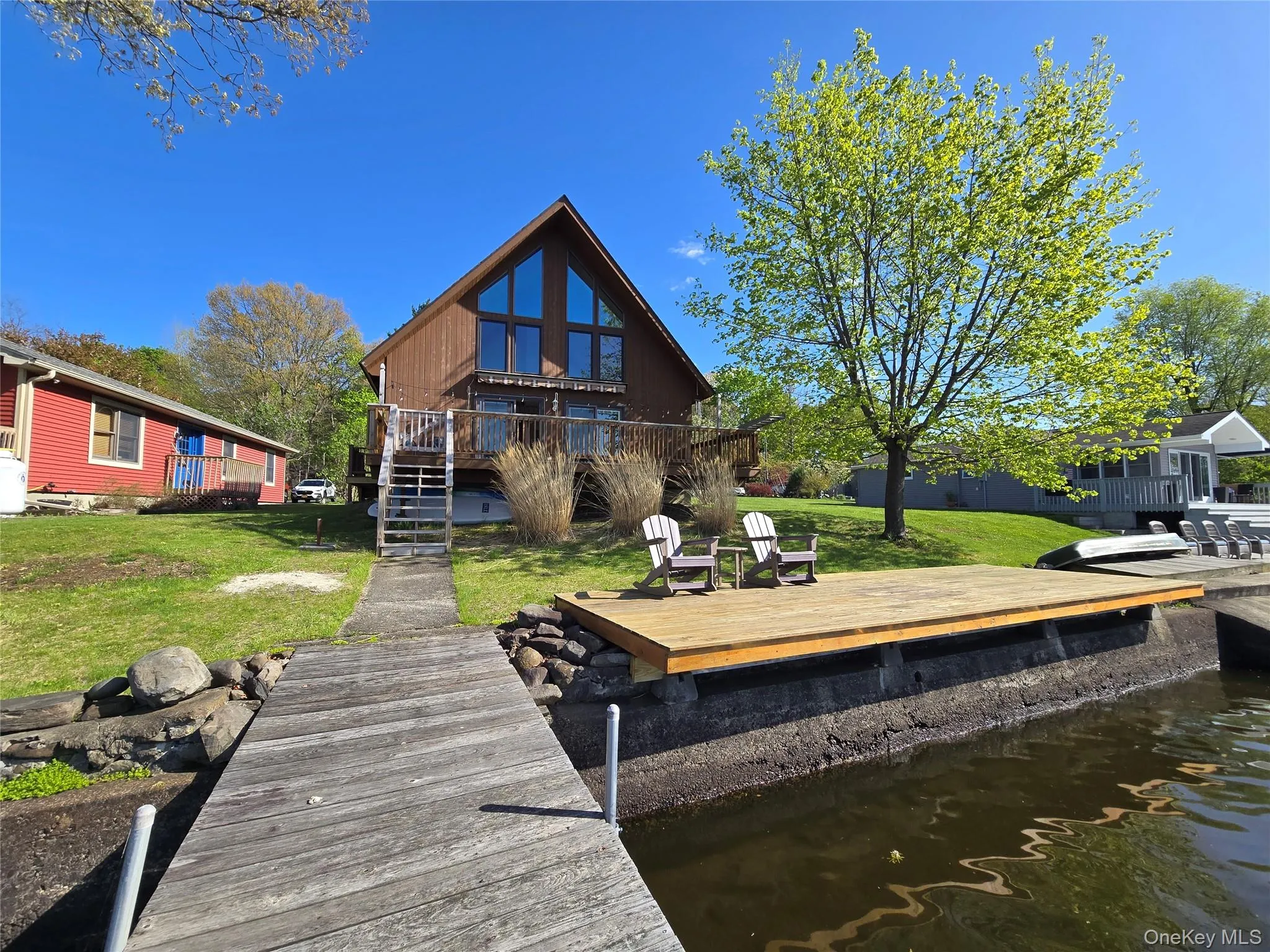 Waterfront property featuring a wood-clad A-frame structure with expansive windows, a multi-level deck, and a private dock Waterfront property featuring a wood-clad A-frame structure with expansive windows, a multi-level deck, and a private dock