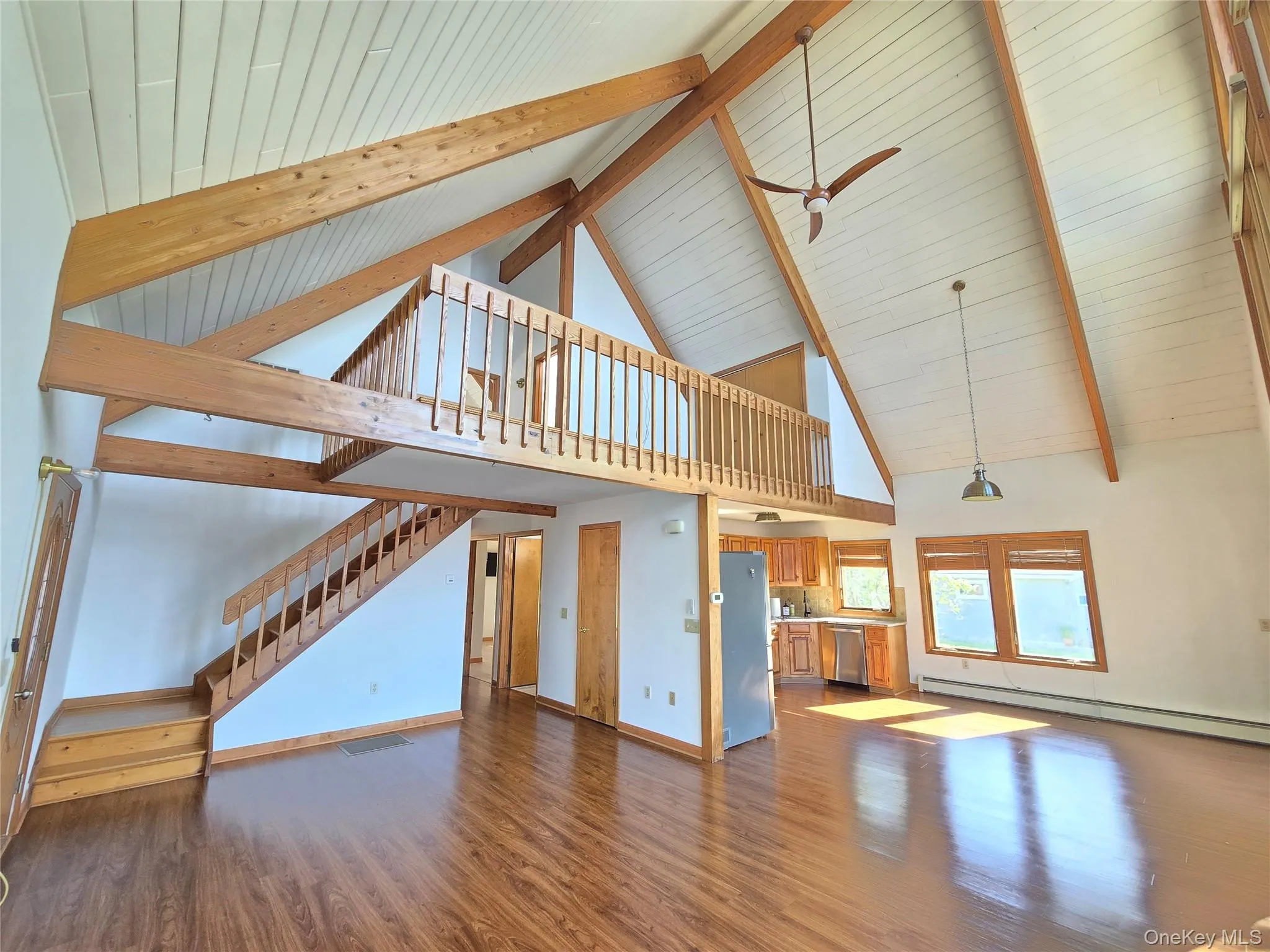 Living Room and kitchen area. Vaulted ceiling with exposed wood beams, wood-finish flooring, and a loft area with wood railing Living Room and kitchen area. Vaulted ceiling with exposed wood beams, wood-finish flooring, and a loft area with wood railing