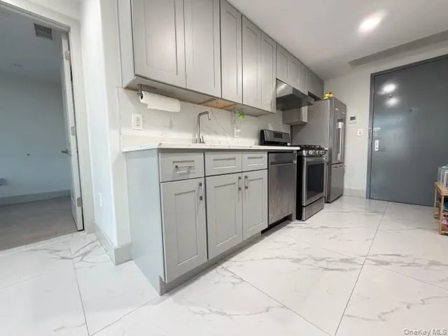 Kitchen featuring gray cabinetry, appliances with stainless steel finishes, light marble finish floors, and under cabinet range hood Kitchen featuring gray cabinetry, appliances with stainless steel finishes, light marble finish floors, and under cabinet range hood