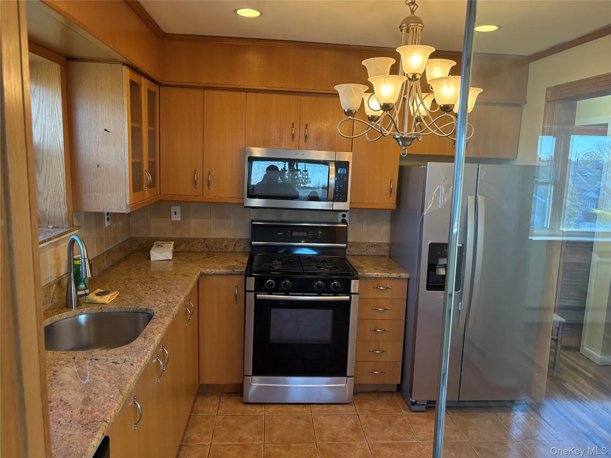 Kitchen featuring stainless steel appliances, light stone counters, a chandelier, glass door, cabinets, and light tile patterned flooring Kitchen featuring stainless steel appliances, light stone counters, a chandelier, glass door, cabinets, and light tile patterned flooring