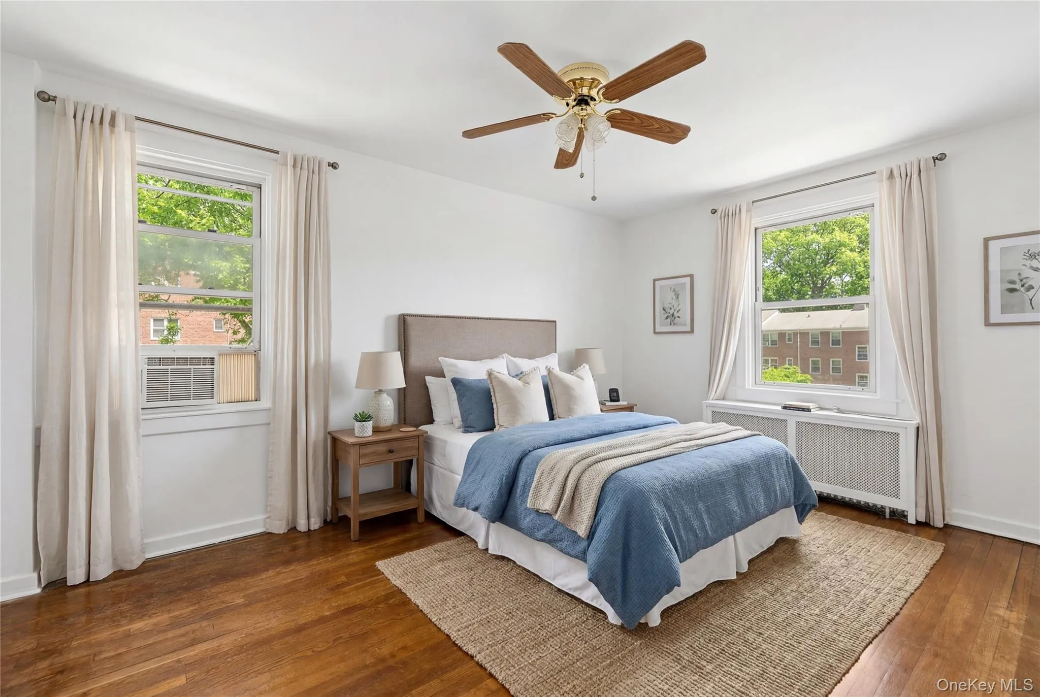 Spacious room featuring wood-finish flooring, white walls, and a ceiling fan with light fixture Spacious room featuring wood-finish flooring, white walls, and a ceiling fan with light fixture