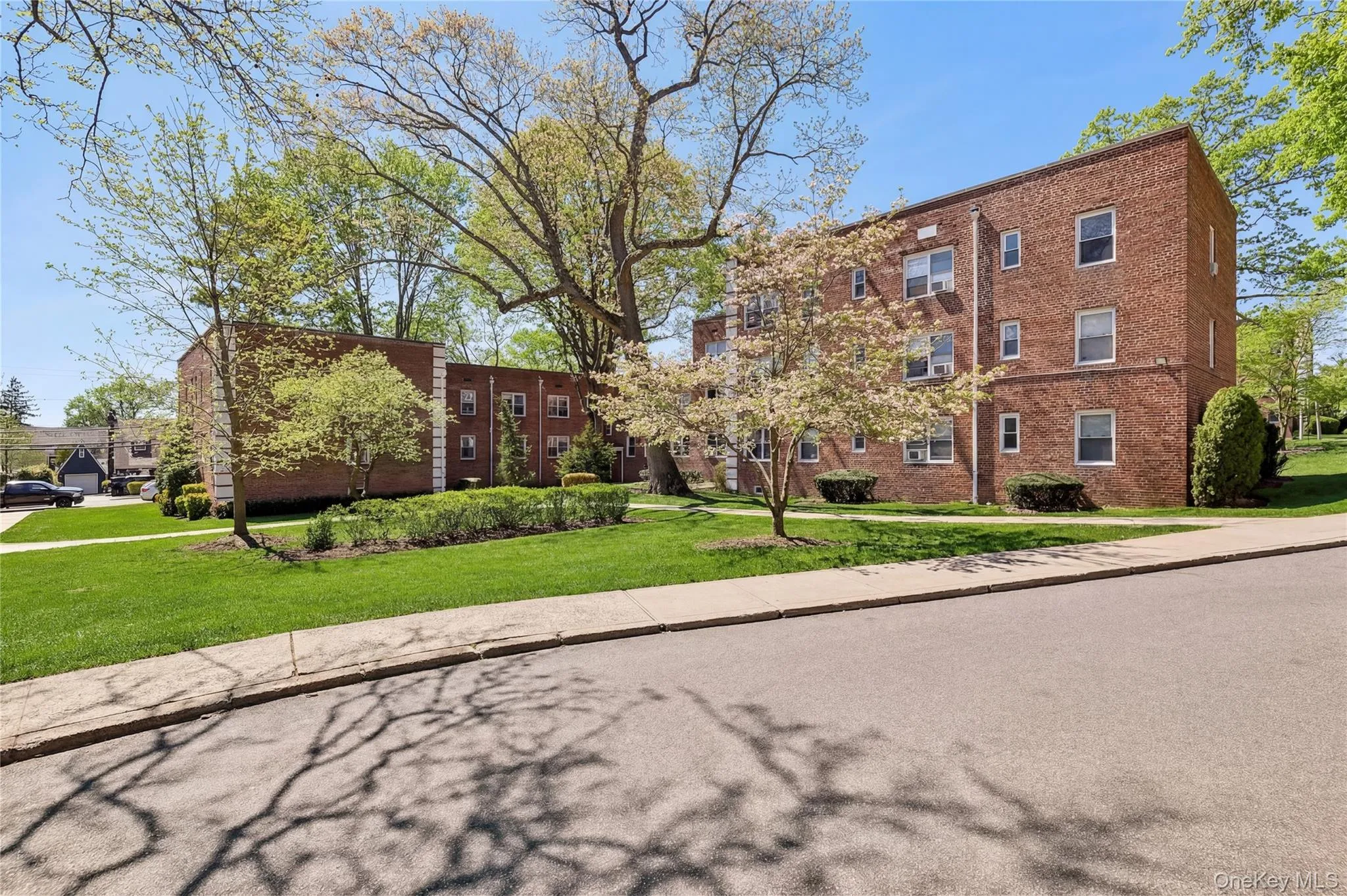 Brick multi-story building featuring multiple windows, mature trees, and landscaped grounds Brick multi-story building featuring multiple windows, mature trees, and landscaped grounds
