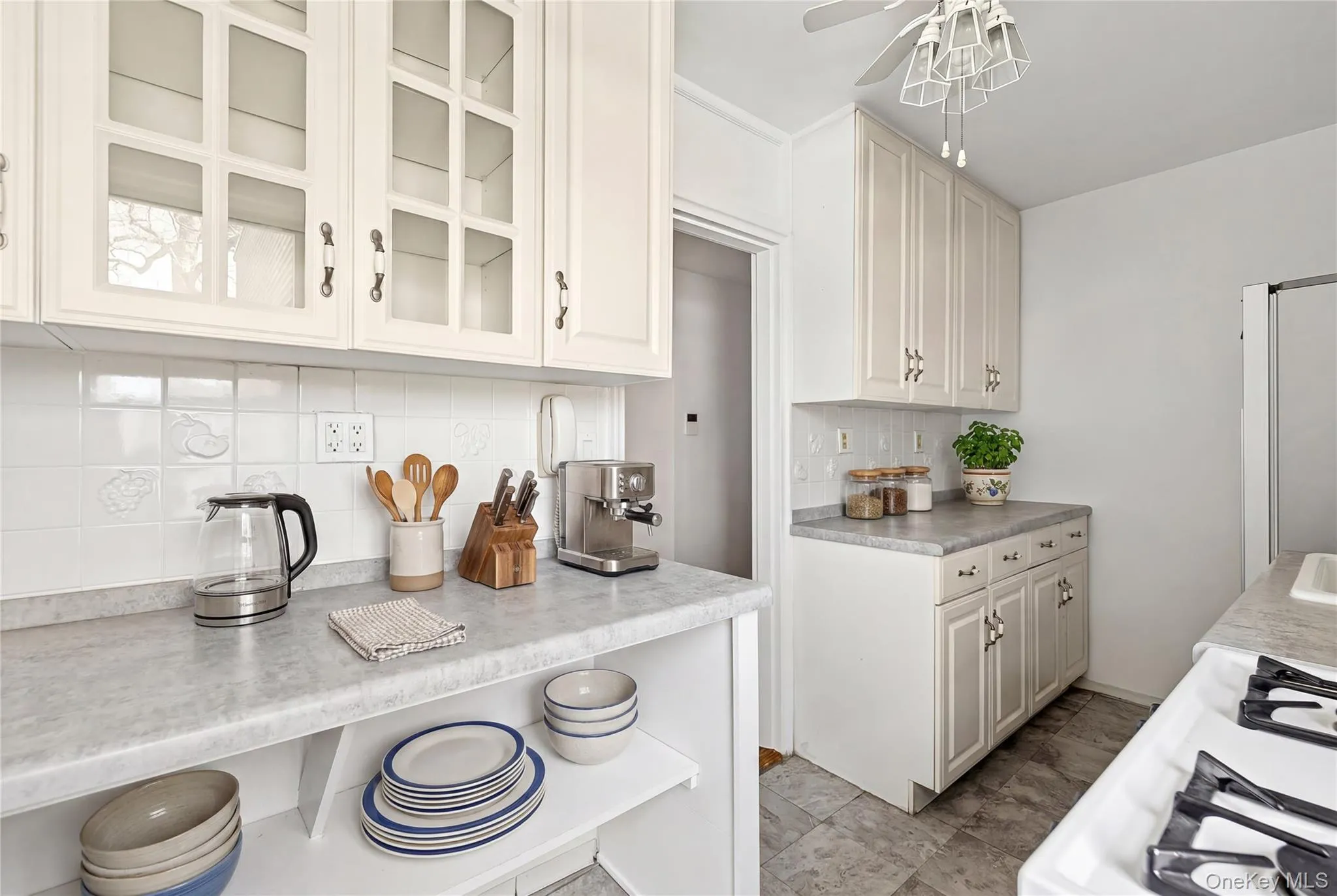 Kitchen featuring light-toned cabinetry with glass-front uppers, patterned tile backsplash, and light-toned countertops Kitchen featuring light-toned cabinetry with glass-front uppers, patterned tile backsplash, and light-toned countertops