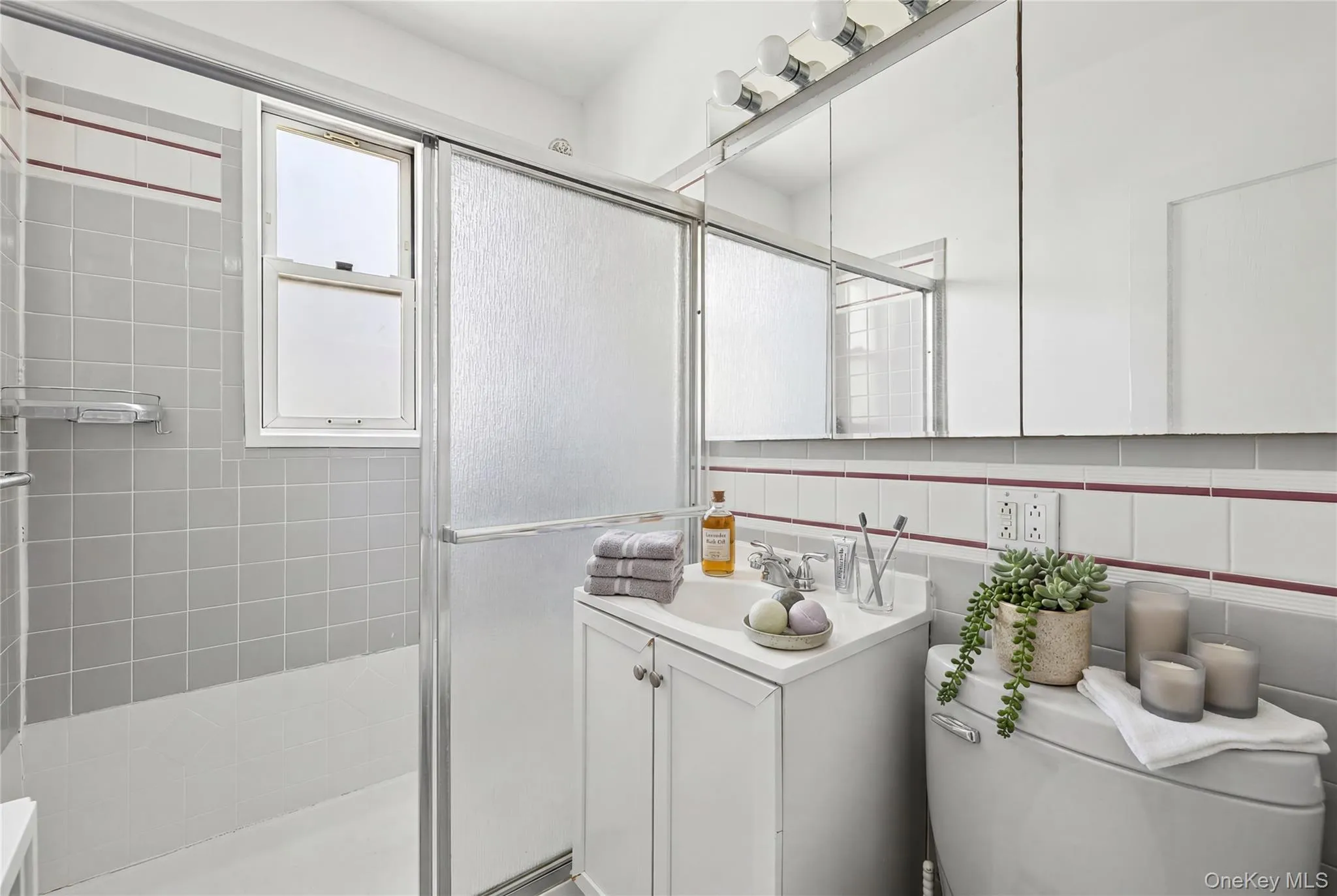 Bathroom featuring a shower-tub combination with sliding glass enclosure, white vanity with integrated sink, and triple mirrored medicine cabinet with overhead lighting Bathroom featuring a shower-tub combination with sliding glass enclosure, white vanity with integrated sink, and triple mirrored medicine cabinet with overhead lighting