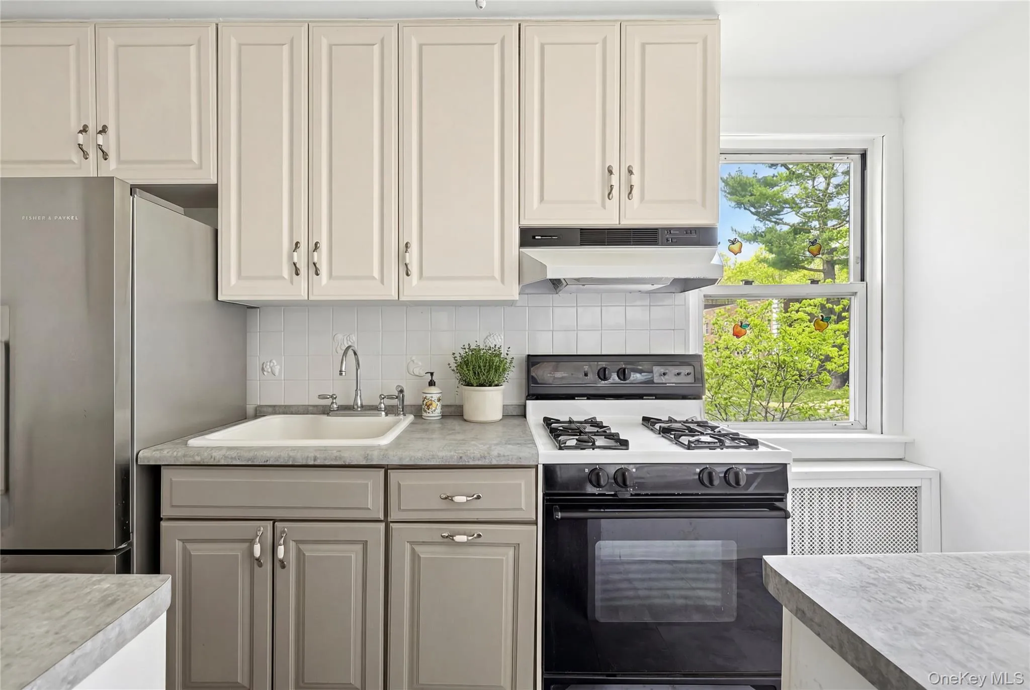 Kitchen featuring a stainless steel refrigerator, white subway tile backsplash, white upper cabinetry, and gray lower cabinetry with coordinating countertops Kitchen featuring a stainless steel refrigerator, white subway tile backsplash, white upper cabinetry, and gray lower cabinetry with coordinating countertops