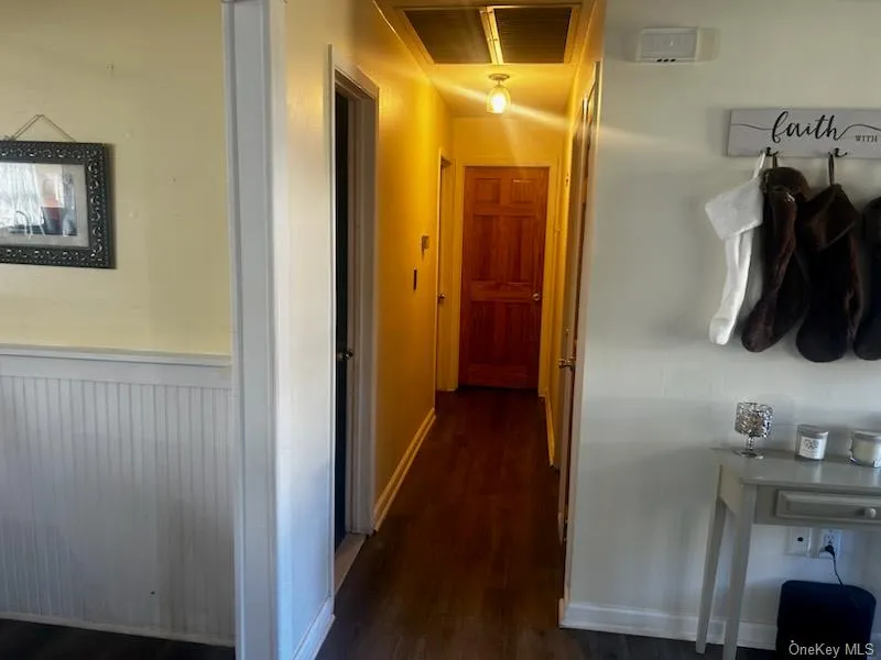 Hallway featuring dark wood finished floors, a wainscoted wall, and visible vents Hallway featuring dark wood finished floors, a wainscoted wall, and visible vents