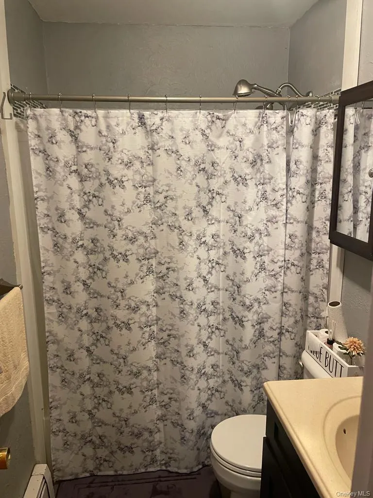 Full bathroom with vanity, a shower with shower curtain, toilet, and a baseboard heating unit Full bathroom with vanity, a shower with shower curtain, toilet, and a baseboard heating unit