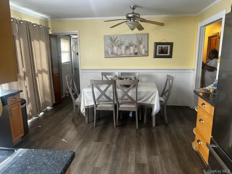 Dining area featuring crown molding, a wainscoted wall, dark wood-style flooring, and ceiling fan Dining area featuring crown molding, a wainscoted wall, dark wood-style flooring, and ceiling fan