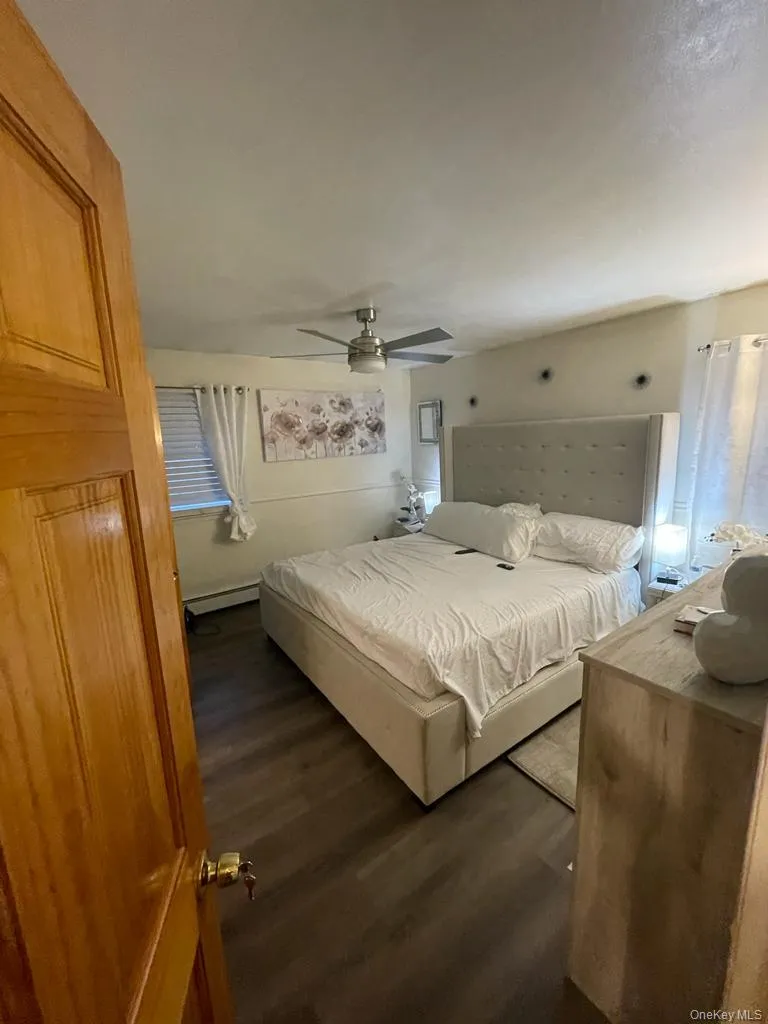 Bedroom featuring dark wood-type flooring, baseboard heating, and ceiling fan Bedroom featuring dark wood-type flooring, baseboard heating, and ceiling fan