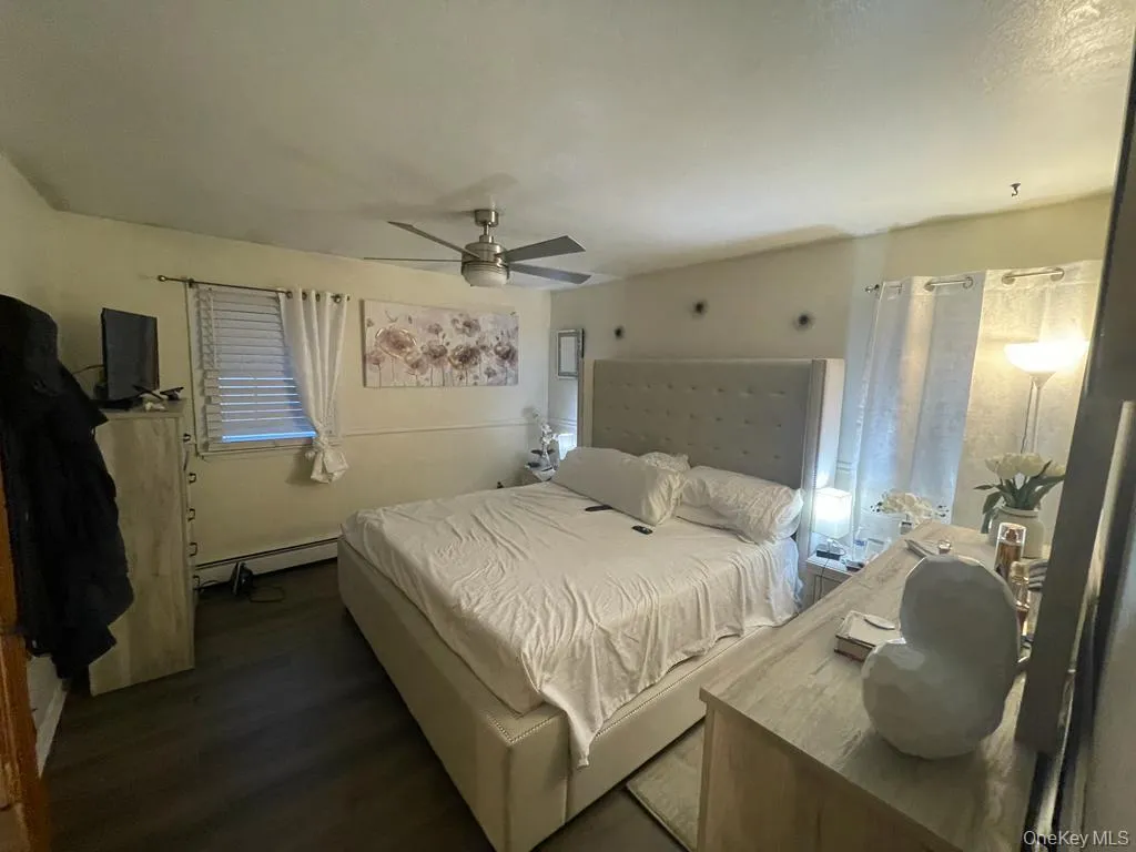 Bedroom featuring ceiling fan, a baseboard radiator, and wood finished floors Bedroom featuring ceiling fan, a baseboard radiator, and wood finished floors