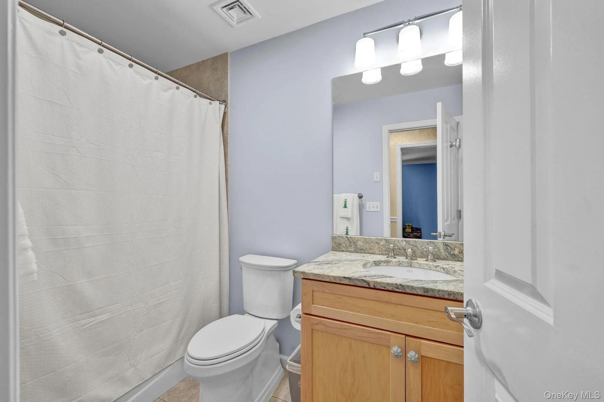 Hallway bathroom featuring a light blue wall, a wood-finish vanity with a stone countertop, an undermount sink, and a wall-mounted light fixture above a mirror Hallway bathroom featuring a light blue wall, a wood-finish vanity with a stone countertop, an undermount sink, and a wall-mounted light fixture above a mirror